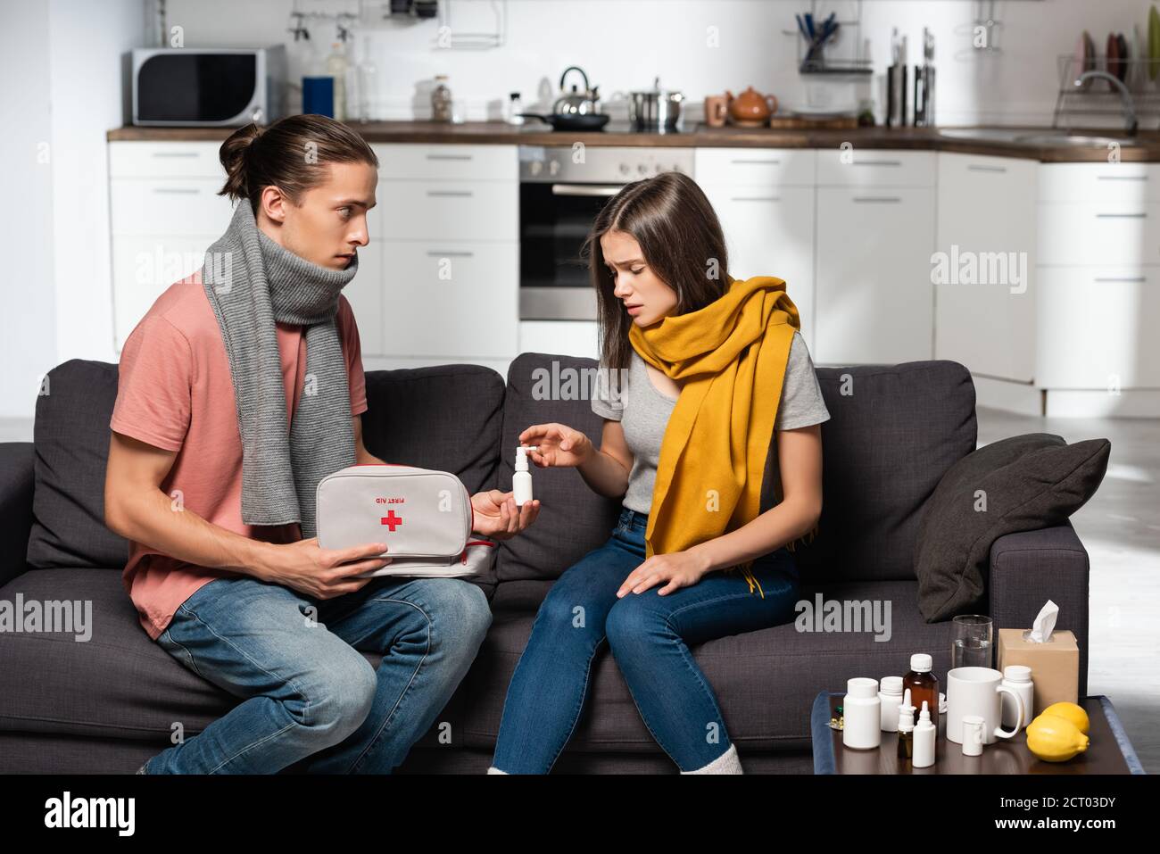 giovane uomo che tiene il capretto di primo soccorso e che dà spray nasale a donna malata in sciarpa calda Foto Stock