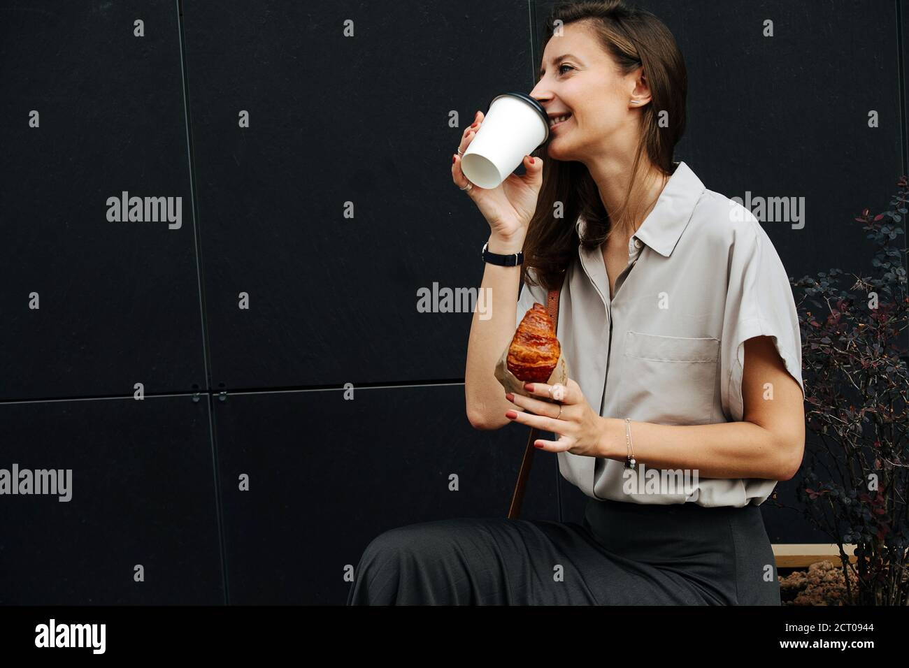 Donna affamata sorridente che beve uno spuntino per strada caffè con croissant Foto Stock