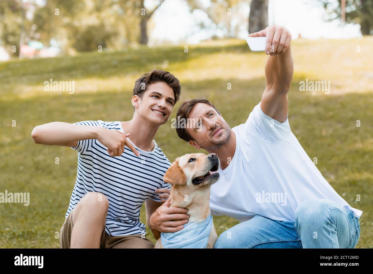 ragazzo adolescente che punta con il dito contro golden retriever mentre padre presa selfie Foto Stock