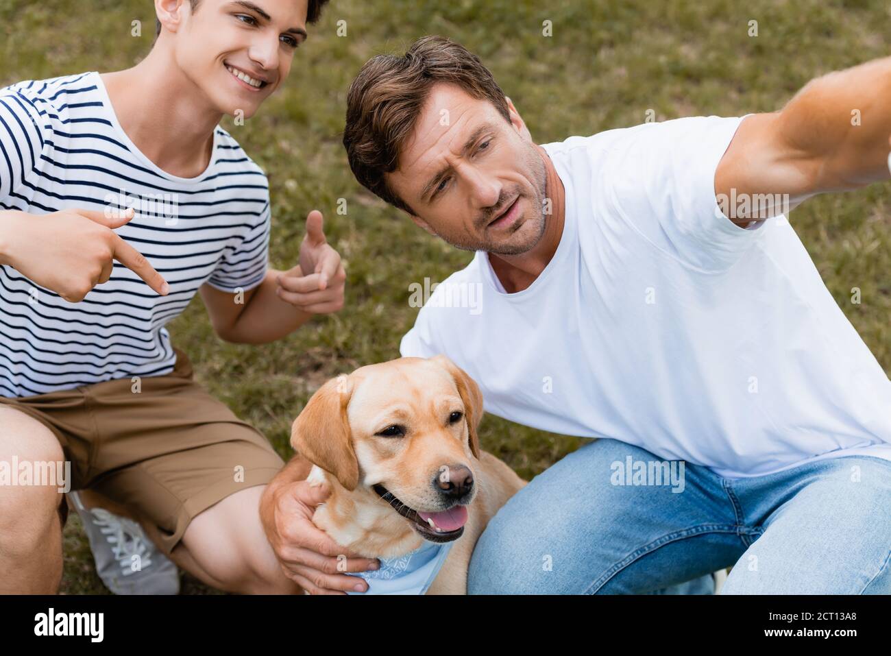 ragazzo adolescente che punta con le dita al retriever d'oro vicino al padre Foto Stock
