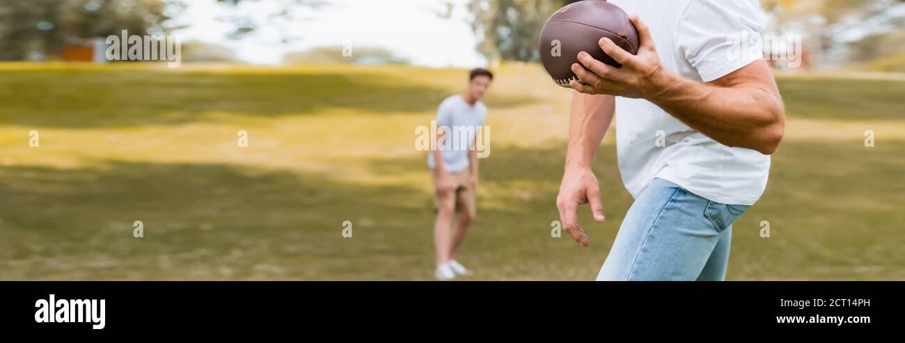 raccolto panoramico di uomo che lancia palla di rugby a figlio dentro parcheggio Foto Stock
