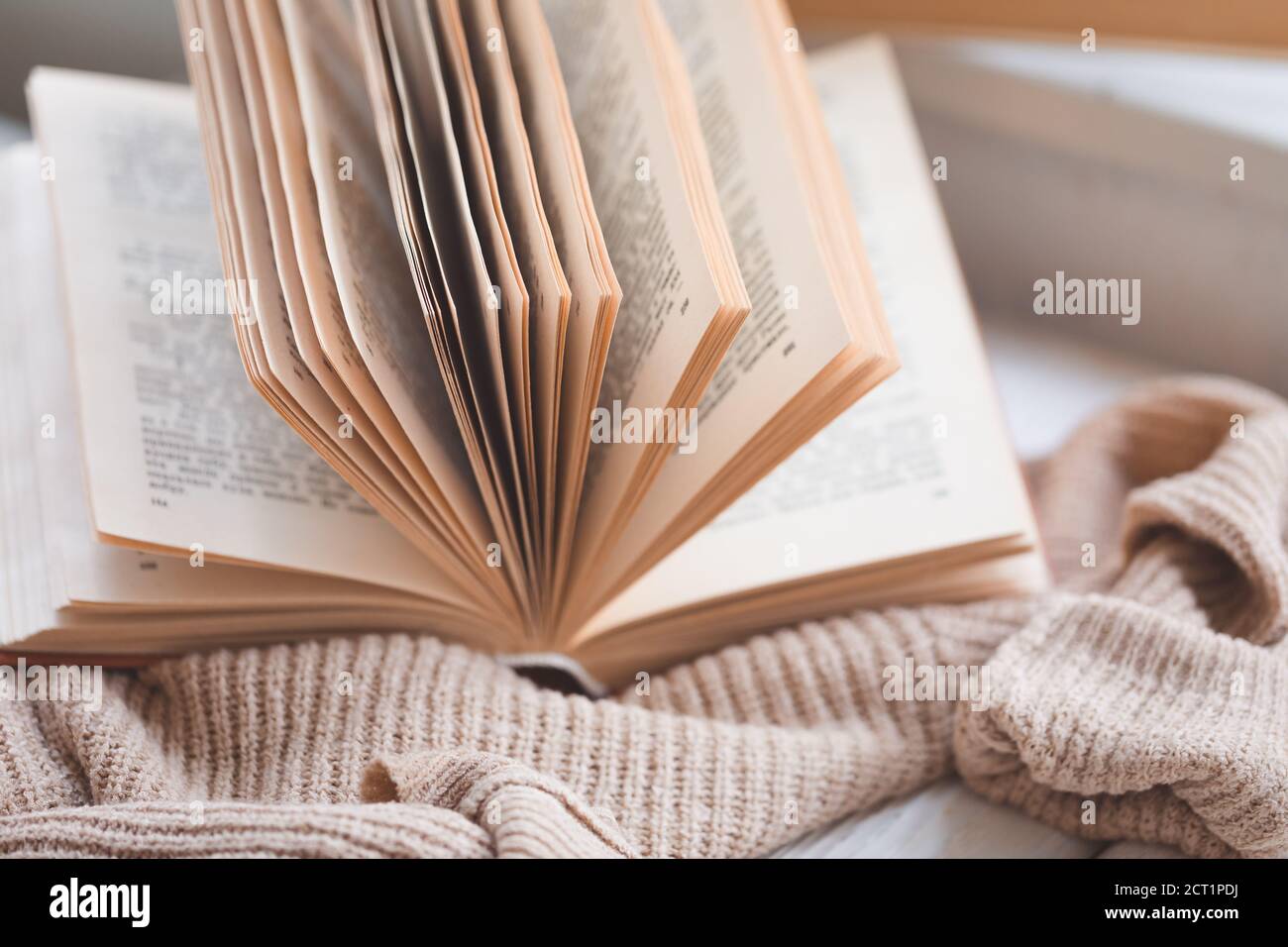 Caldo e accogliente Hygge concetto con bianco e beige maglione, vecchio libro aperto su un davanzale, tonato Foto Stock