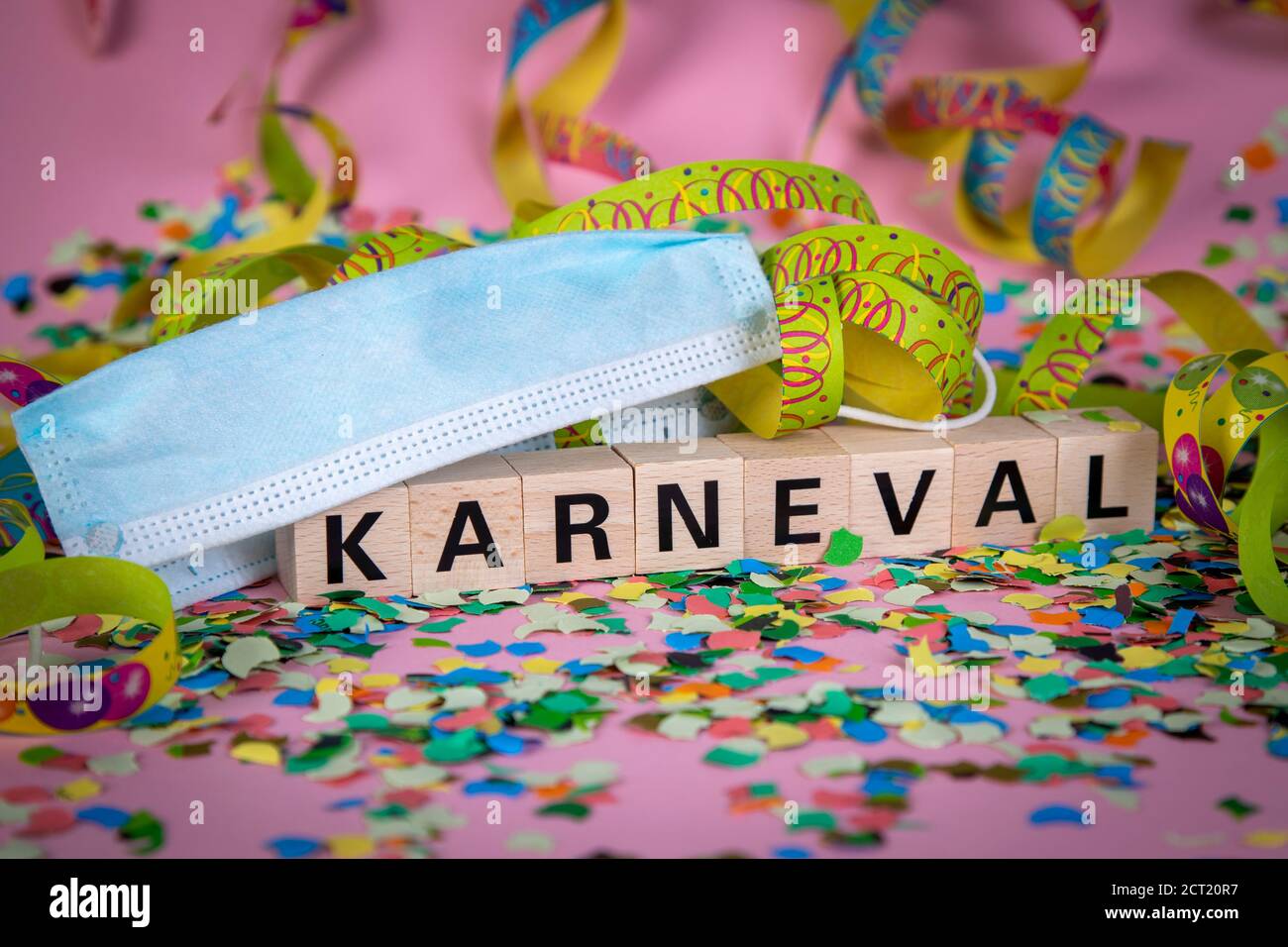 Parola tedesca KARNIVAL su blocchi di legno sotto una maschera viso con confetti e streamers, sfondo rosa Foto Stock