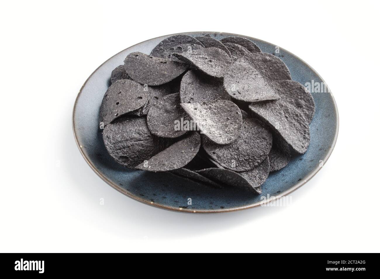Patatine nere con carbone su una piastra di ceramica blu isolata su sfondo bianco. Vista laterale, primo piano. Foto Stock