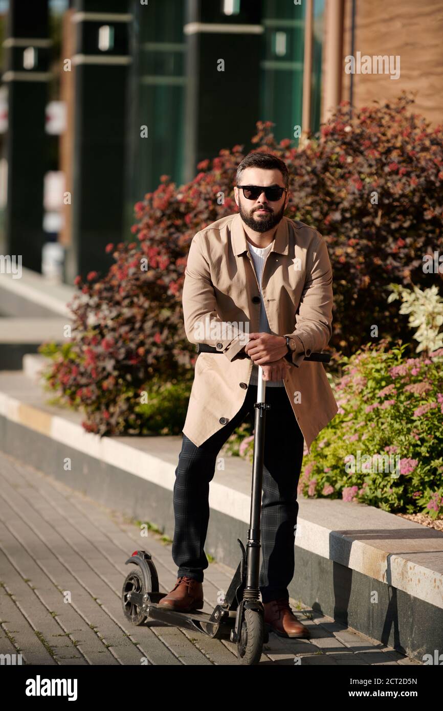 Giovane uomo d'affari sopportato in occhiali da sole appoggiati su maniglie di elettrico scooter Foto Stock
