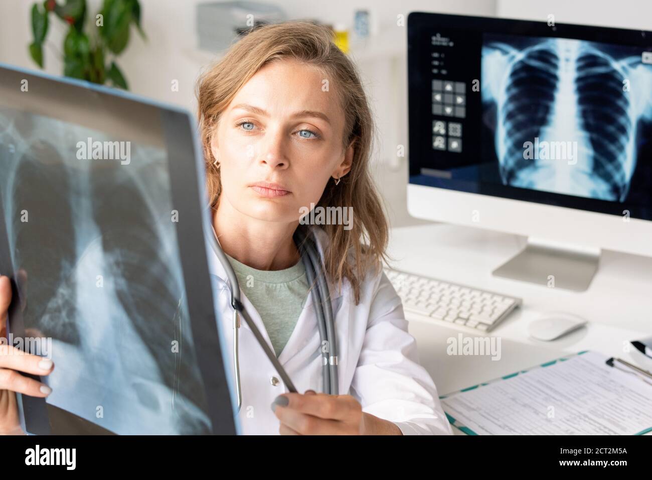Radiologo femminile giovane e serio nel whitecoat che punta all'immagine radiografica di polmoni Foto Stock