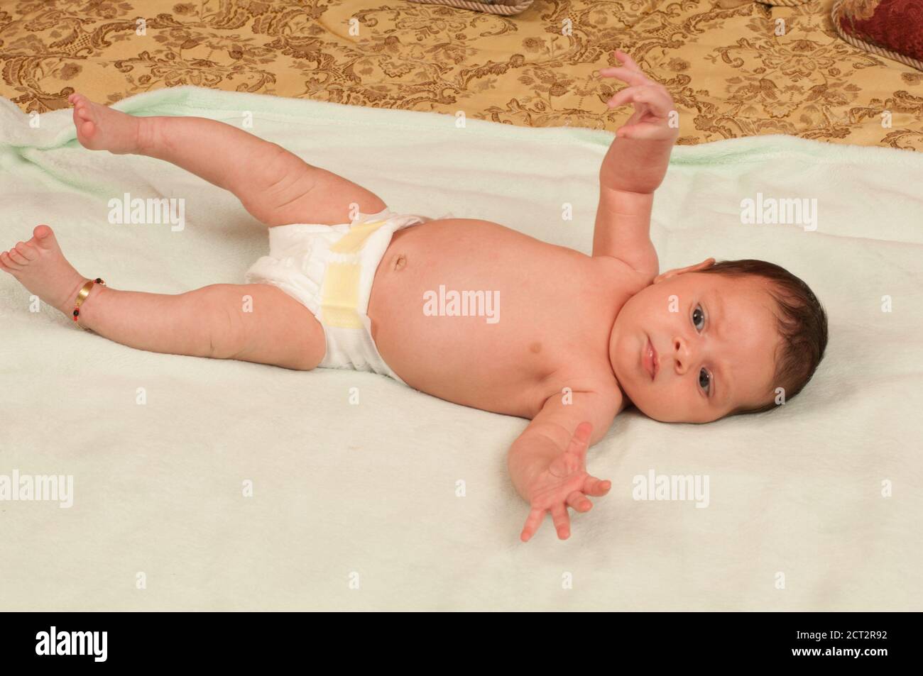 Bambina neonato di 1 mese sulla schiena in pannolino, riflesso startle (riflesso Moro), caviglia per fortuna Foto Stock