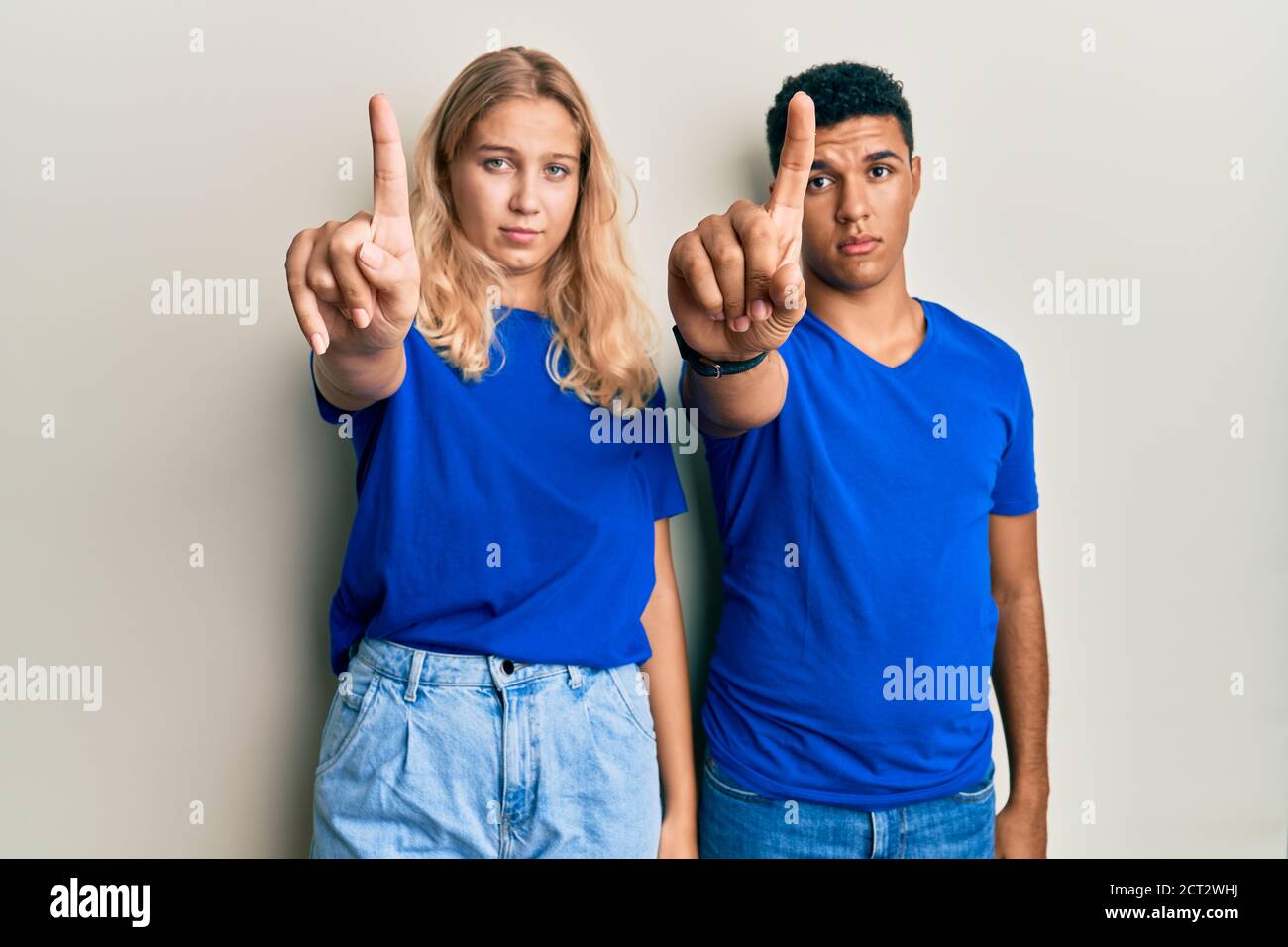 Giovane coppia interracial che indossa abiti casual puntando con il dito verso l'alto e l'espressione arrabbiata, non mostrando alcun gesto Foto Stock