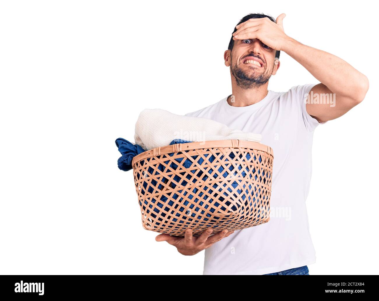 Giovane bell'uomo che tiene il cesto di bucato stressato e frustrato con la mano sulla testa, sorpreso e faccia arrabbiata Foto Stock