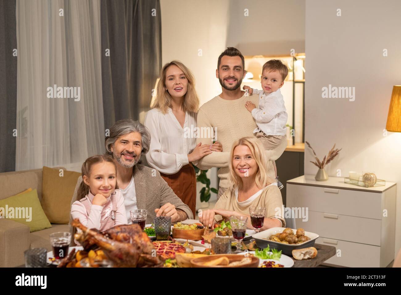 Felice famiglia contemporanea di tre generazioni che vi guarda con sorrisi Foto Stock