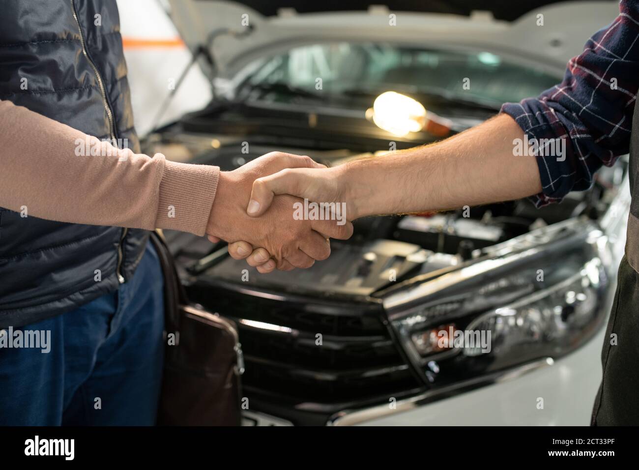 Giovane tecnico contemporaneo di servizio auto scuotendo mano di maschio cliente Foto Stock