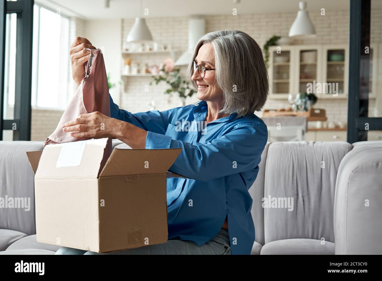 Felice metà invecchiata donna apertura pacco disimballaggio postale consegna scatola a casa. Foto Stock