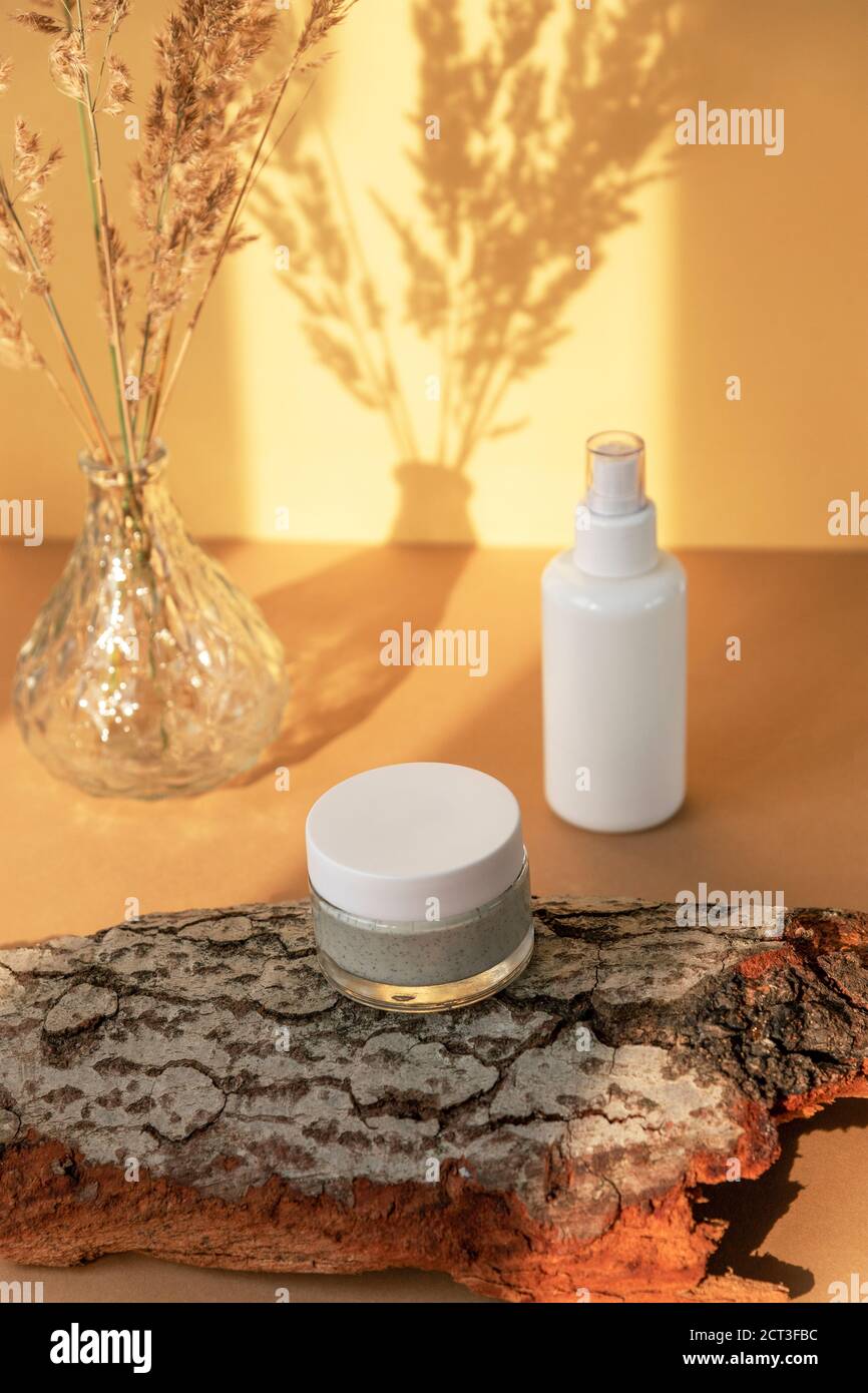 Prodotti per la cura della pelle sulla corteccia naturale dell'albero alla luce del sole contro una parete gialla. Trattamenti di bellezza biologici. Messa a fuoco selettiva Foto Stock