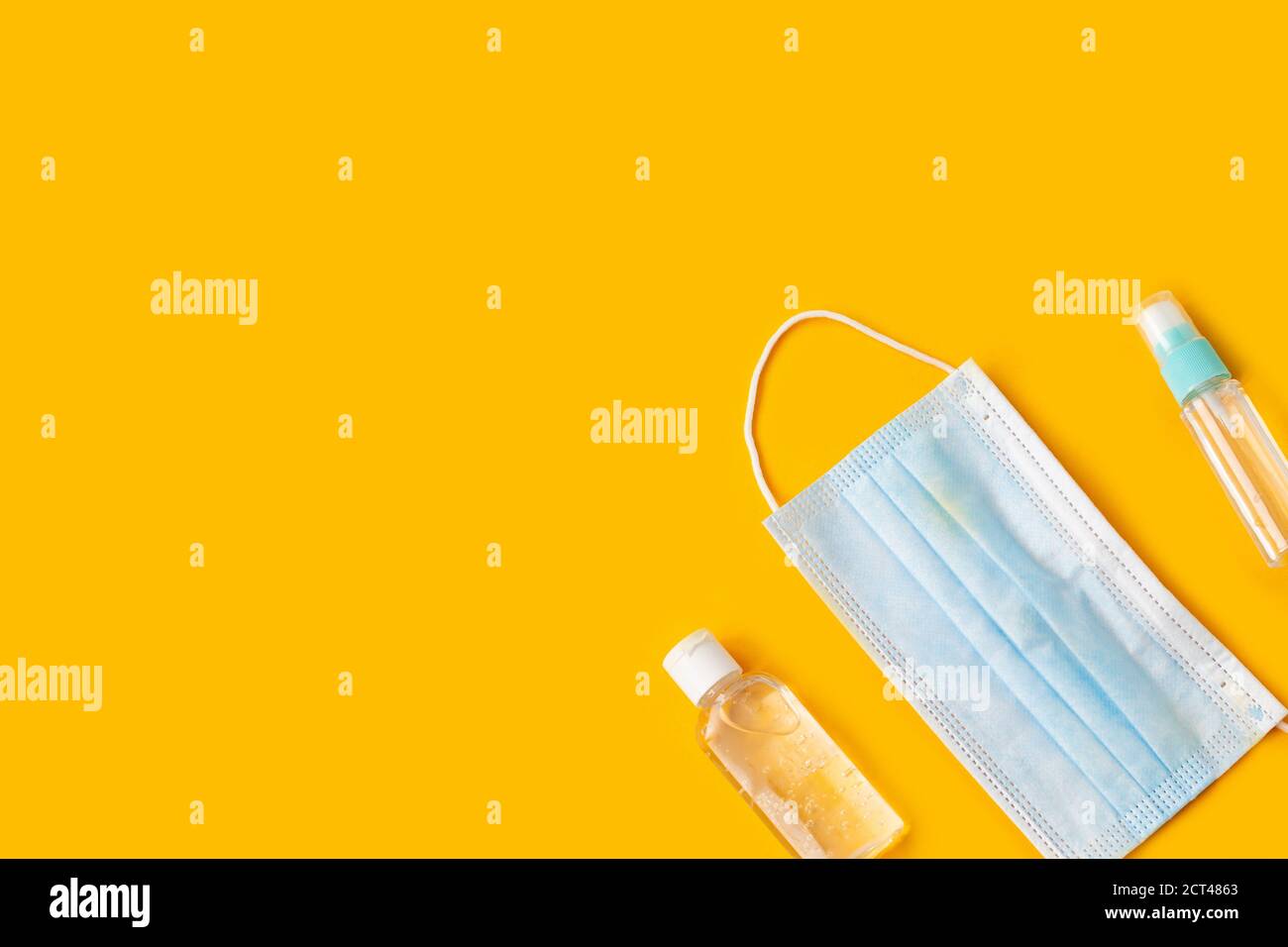 Maschere facciali e bottiglie igienizzanti per le mani su sfondo giallo. Foto Stock