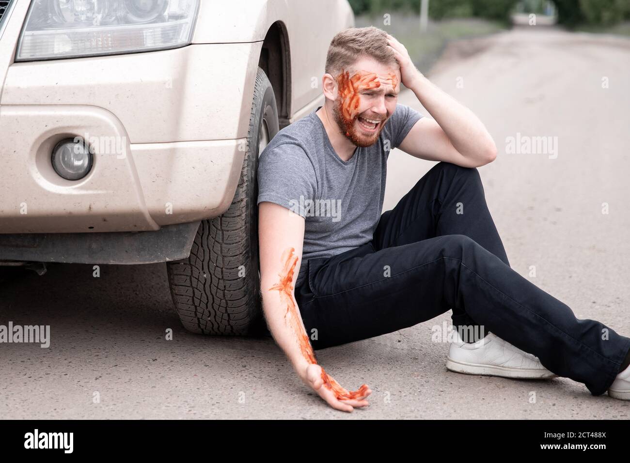 Il giovane si siede con la testa sanguinata vicino alla ruota dell'automobile, urlando e rammaricandosi atto Foto Stock