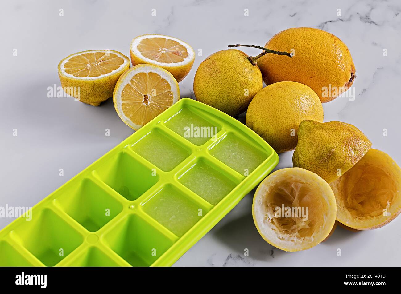 Limoni interi e dimezzati, parzialmente spremuti e il succo versato in contenitori di cubetti di ghiaccio Foto Stock