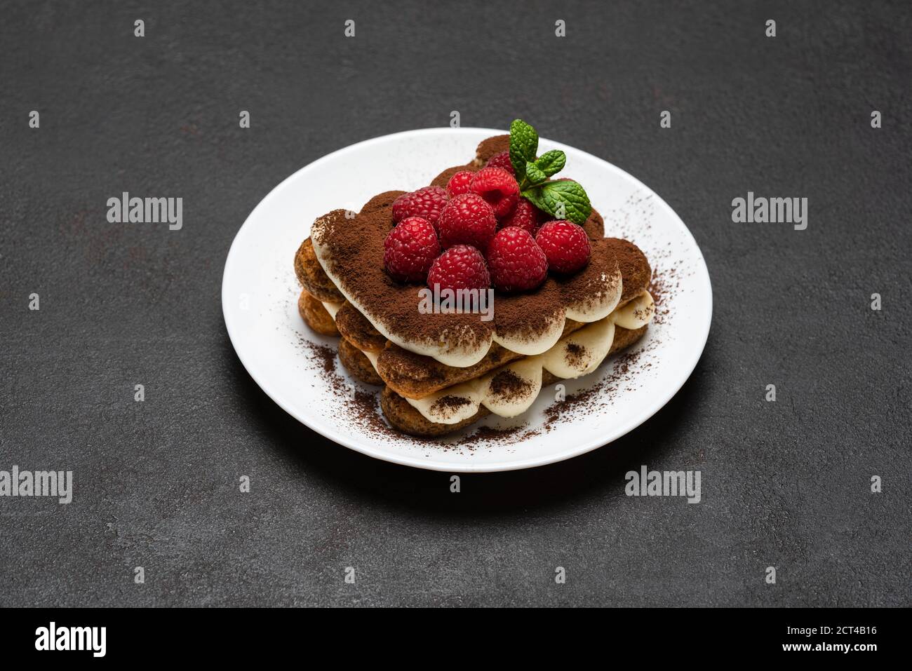 Porzione di dessert classico tiramisù con lamponi su cemento scuro sfondo Foto Stock