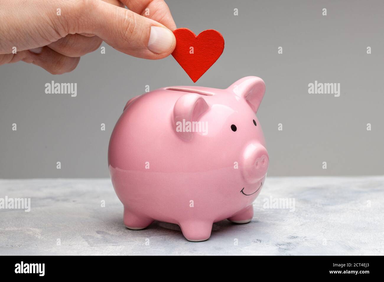 Donatore. Un uomo tiene un cuore rosso in mano e va alla banca del piggy come donazione. Sfondo grigio. Foto Stock