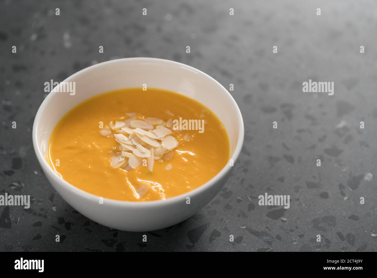 Purea di zuppa di zucca decorata con scaglie di mandorle in ciotola bianca su fondo di cemento, fuoco basso Foto Stock