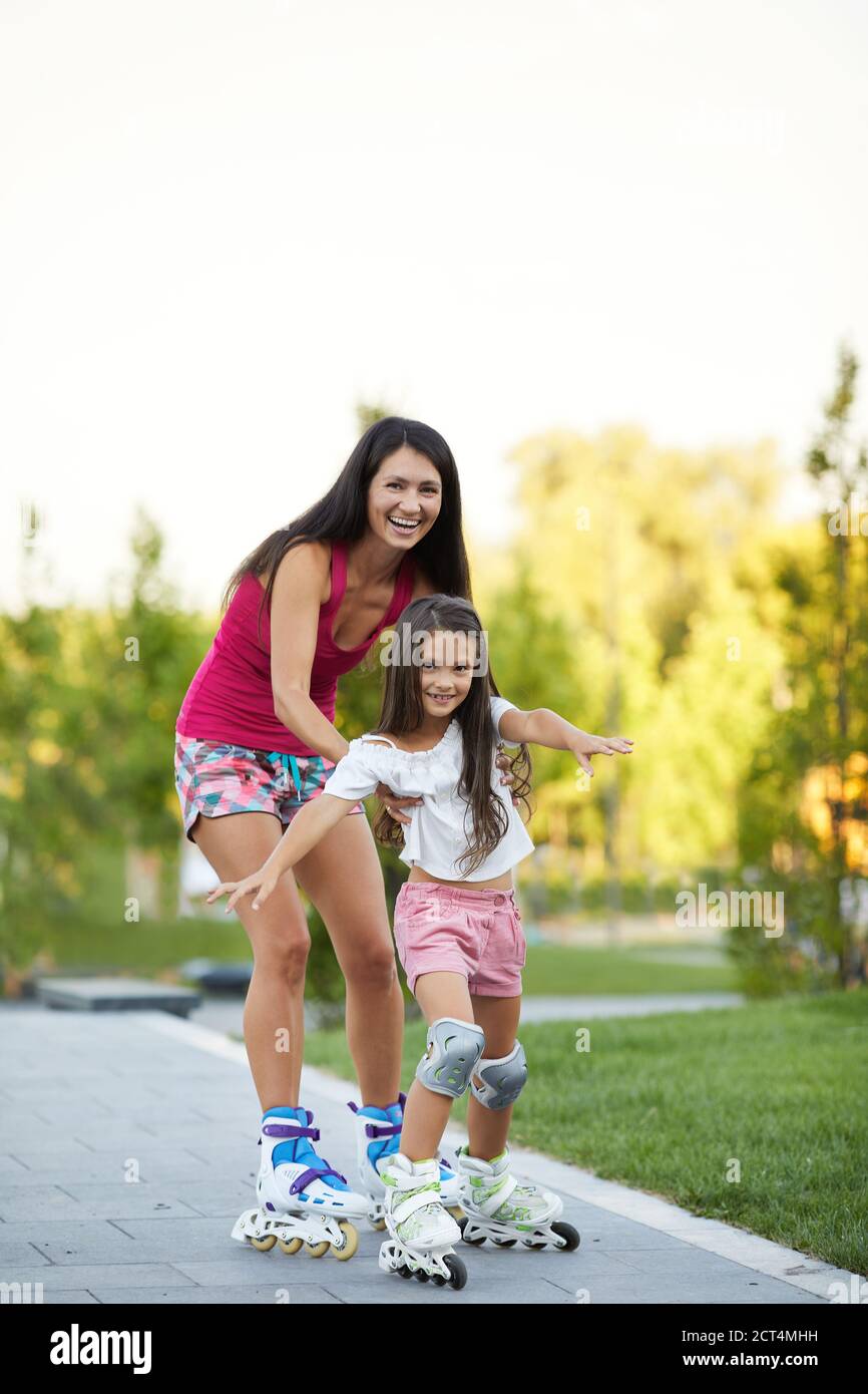 bella madre sta insegnando alla sua piccola figlia a pattinare sul pattinaggio a rotelle nel parco. felice famiglia Foto Stock