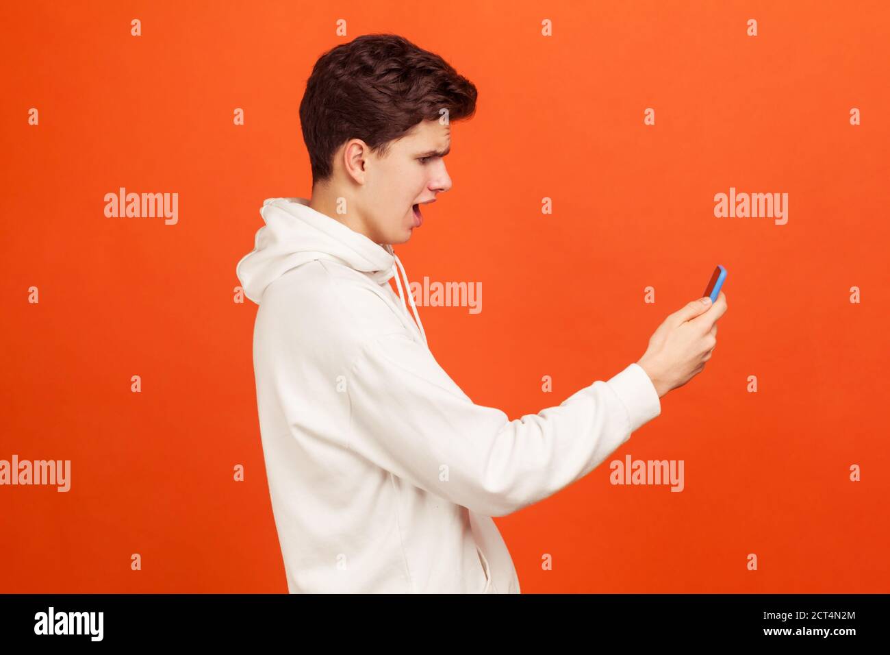 Profilo ritratto di un adolescente scioccato in bianco casual felpa guardando lo schermo del telefono cellulare con il volto eccitato, la ricezione di e-mail con buoni di vendita Foto Stock