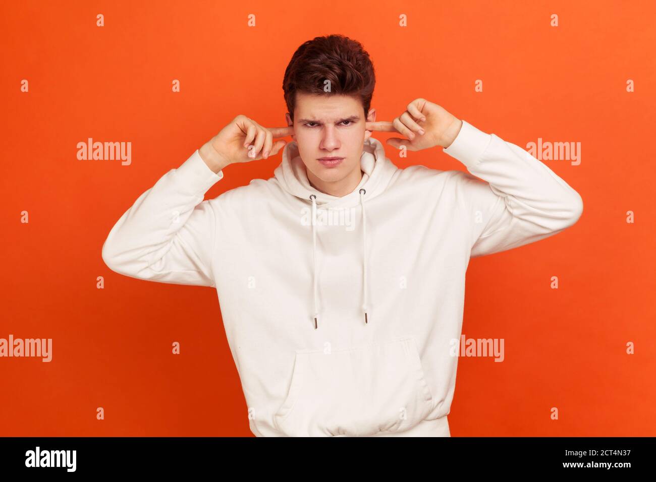 Non voglio sentir! Adolescente arrabbiato in elegante felpa con cappuccio che chiude le orecchie con le dita, disobbedienza, ignorando fastidioso rumore. Studio interno Sho Foto Stock