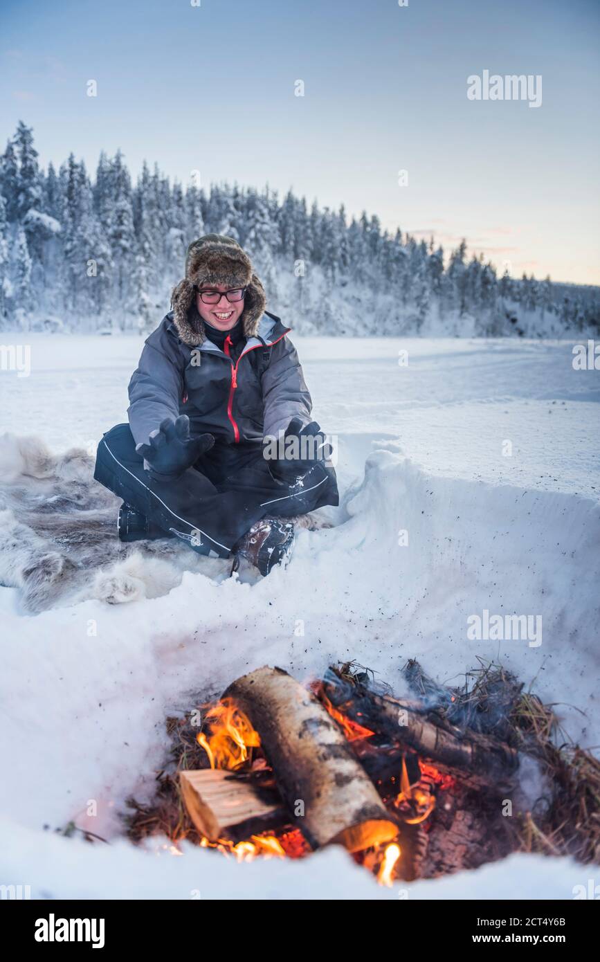 In inverno, nel Circolo polare Artico di Lapponia, in Finlandia, una persona si sedette a un fuoco di campo che si riscaldava in una fredda giornata Foto Stock