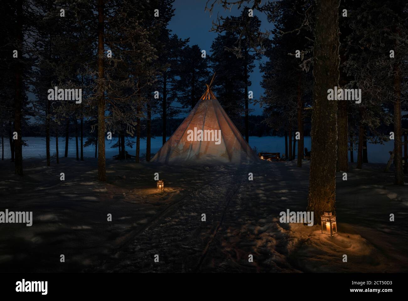Esperienza di viaggio unica di campeggio in una tenda campanaria Kota nella foresta in un paesaggio invernale coperto di neve con candele di notte in Lapponia, Finlandia, Circolo polare Artico Foto Stock