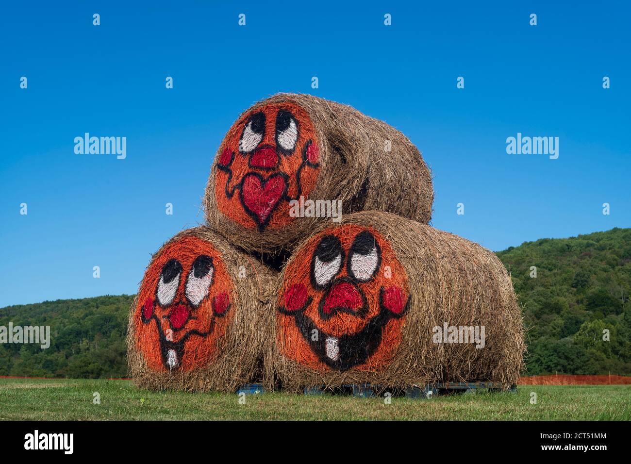 Tre barili di fieno rotolati che sono accatastati in una piramide la forma con le facce verniciate del cartone animato si trova al centro di un campo in una giornata di sole senza clou Foto Stock