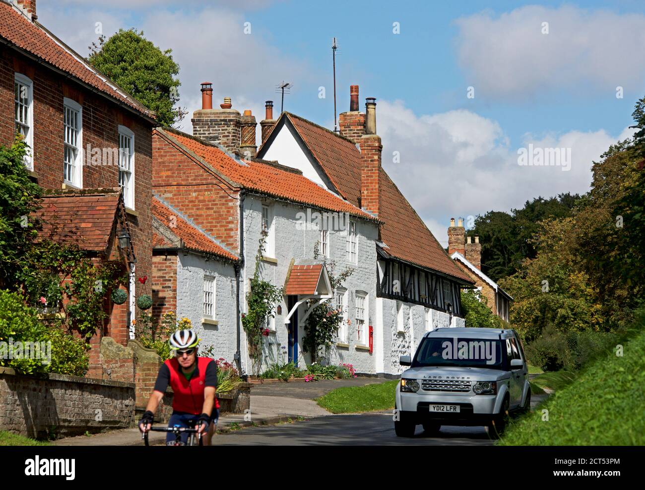 Ciclista e Range Rover passando per il vecchio ufficio postale nel villaggio di Dalton Sud, East Yorkshire, Inghilterra Regno Unito Foto Stock