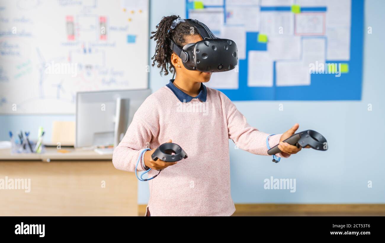 Scuola elementare computer Science Class: Cute Girl indossare Augmented Reality Headset e l'utilizzo di Controller impara le lezioni in realtà virtuale eccitato Foto Stock