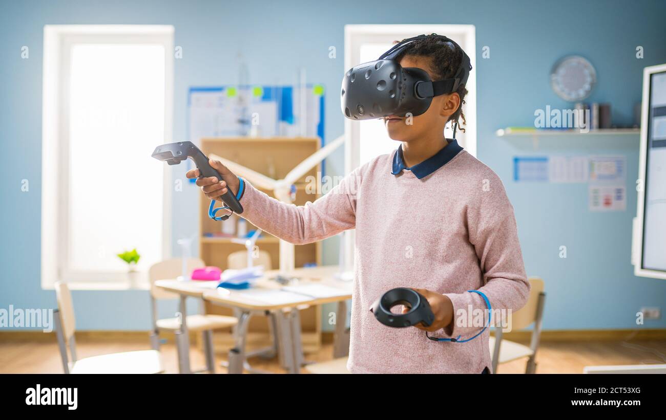 Scuola elementare computer Science Class: Cute Girl indossare Augmented Reality Headset e l'utilizzo di Controller impara le lezioni in realtà virtuale eccitato Foto Stock
