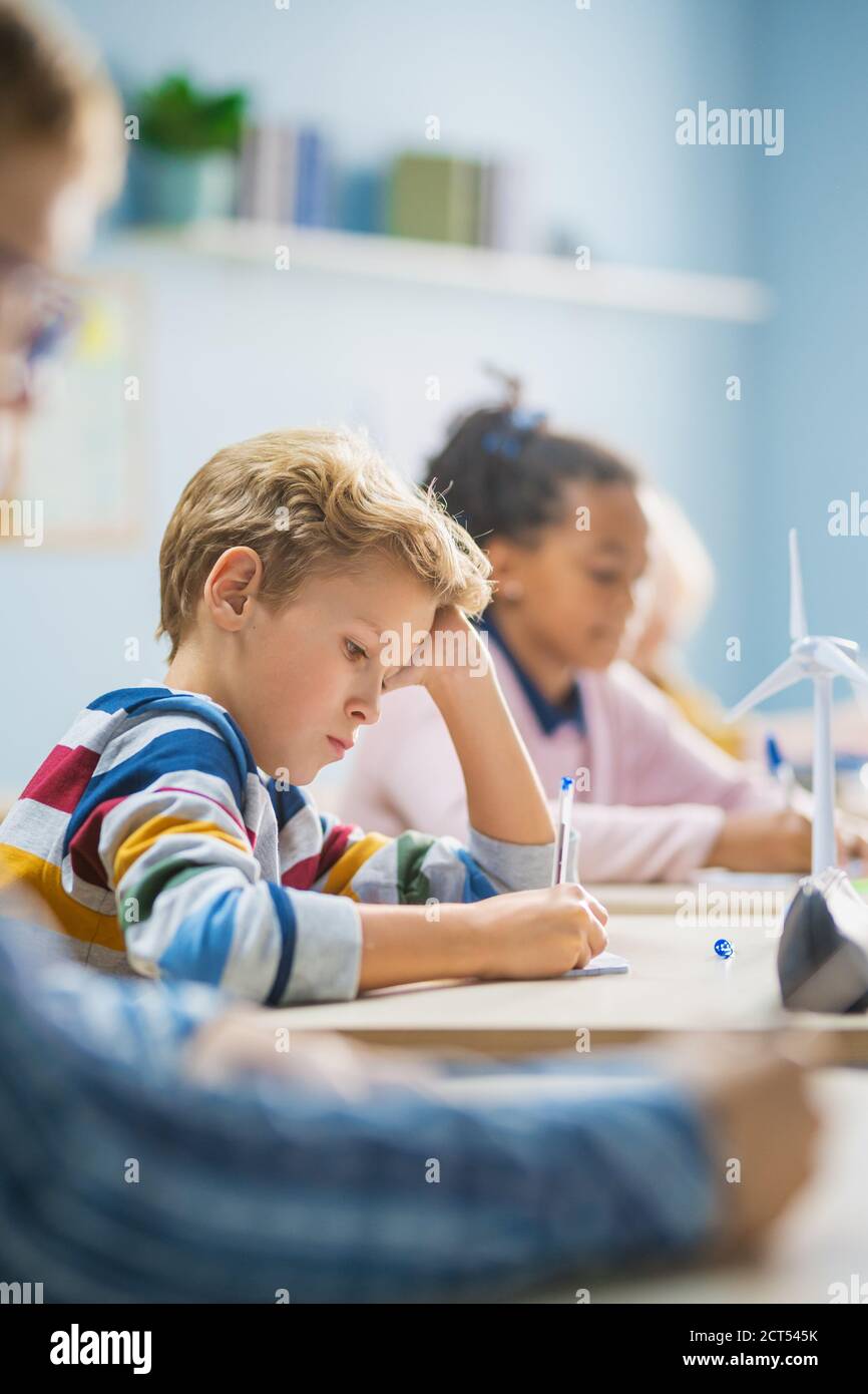 In classe scuola elementare Brilliant caucasic Boy scrive in Eserctaccuino, prendendo prova e scrivendo esame. Classe Junior con gruppo di Foto Stock