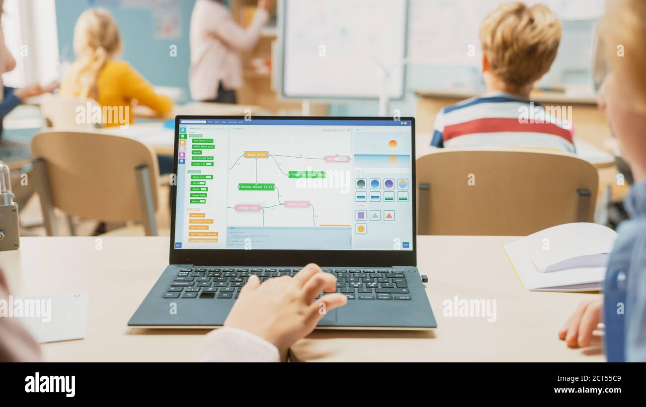 Scuola elementare Scienza Classe: Sopra la spalla Little Boy e Girl uso laptop con schermo che mostra software di programmazione. Spiega l'insegnante di fisica Foto Stock