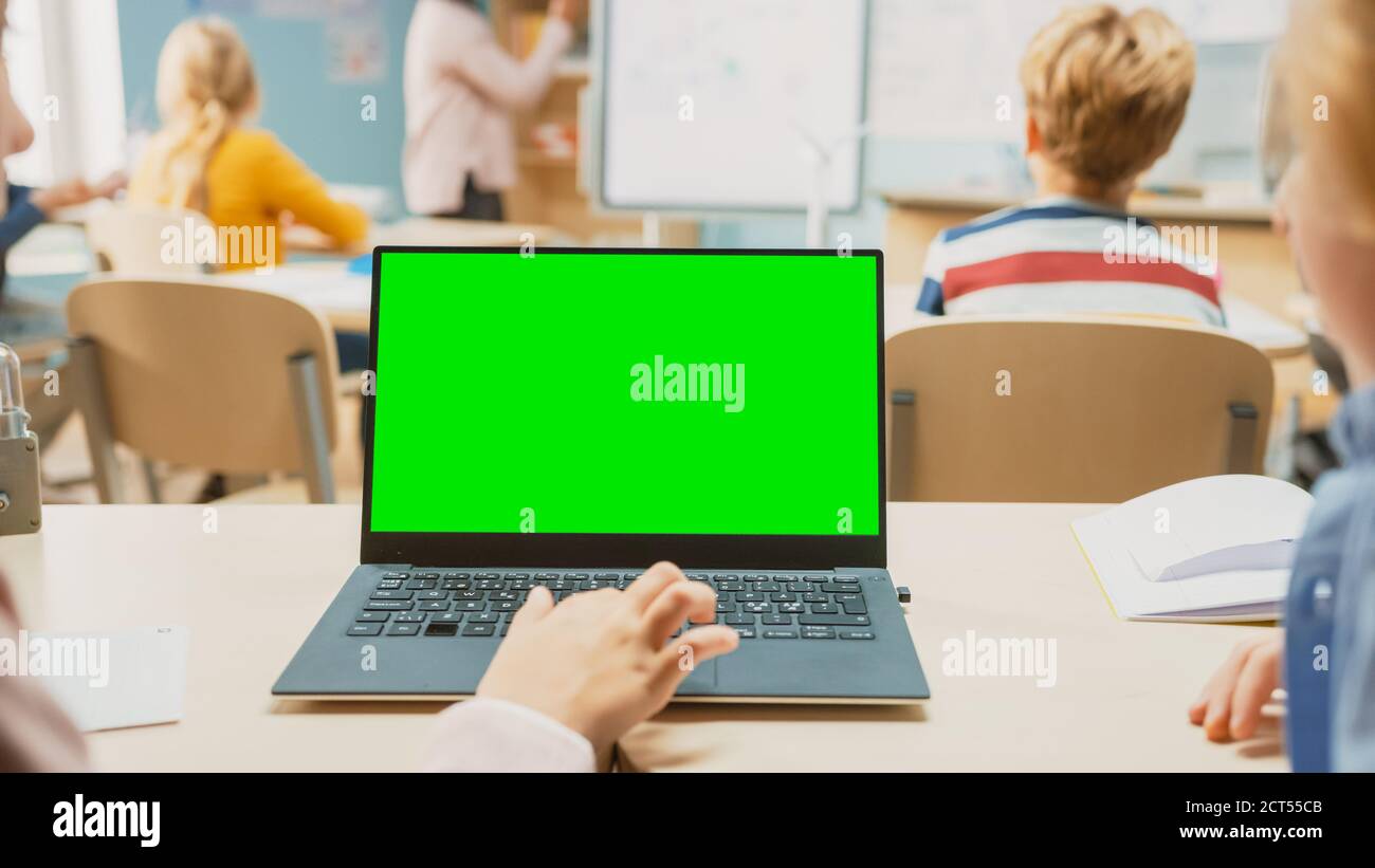 Classe di scienza della scuola elementare: Laptop di uso della piccola ragazza con modello di mock-up dello schermo verde. Nella classe della scuola di fondo piena di diversi Smart Kids Foto Stock