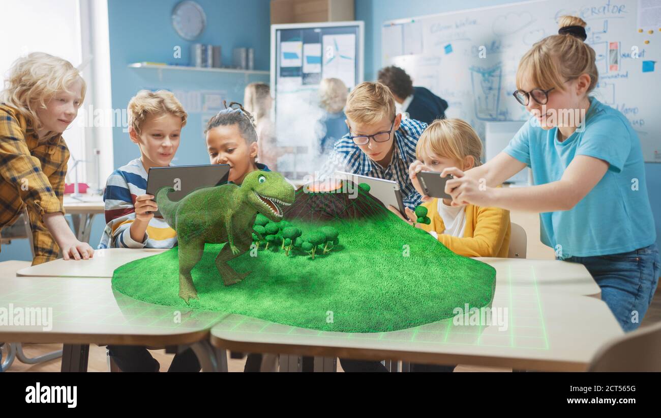 Gruppo di bambini della scuola usano i calcolatori digitali del tablet con l'applicazione di realtà aumentata, guardando l'animazione 3D educativa - camminata dei dinosauri sull'isola Foto Stock
