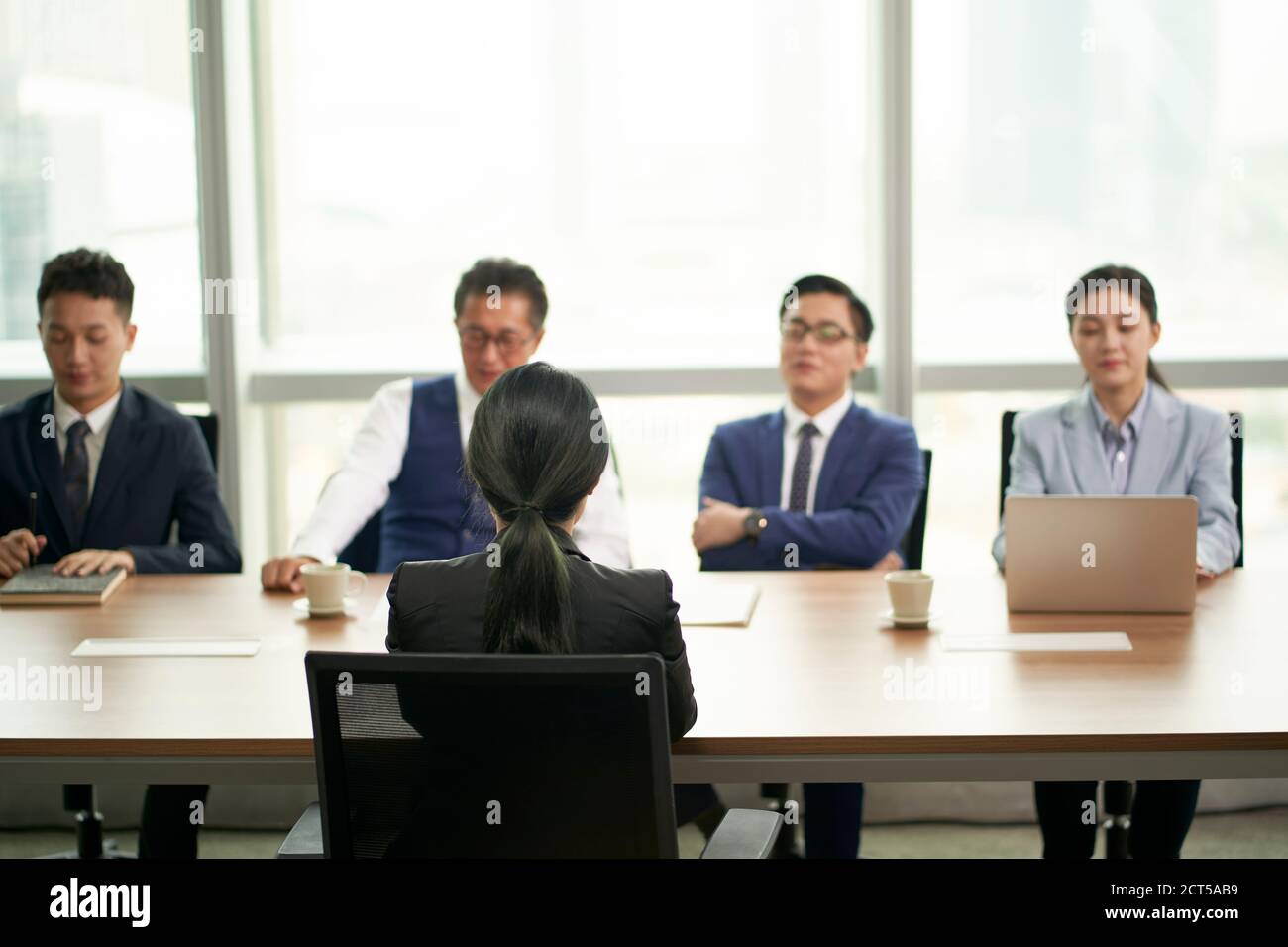 giovane donna asiatica d'affari intervistata da un gruppo di dirigenti aziendali Foto Stock