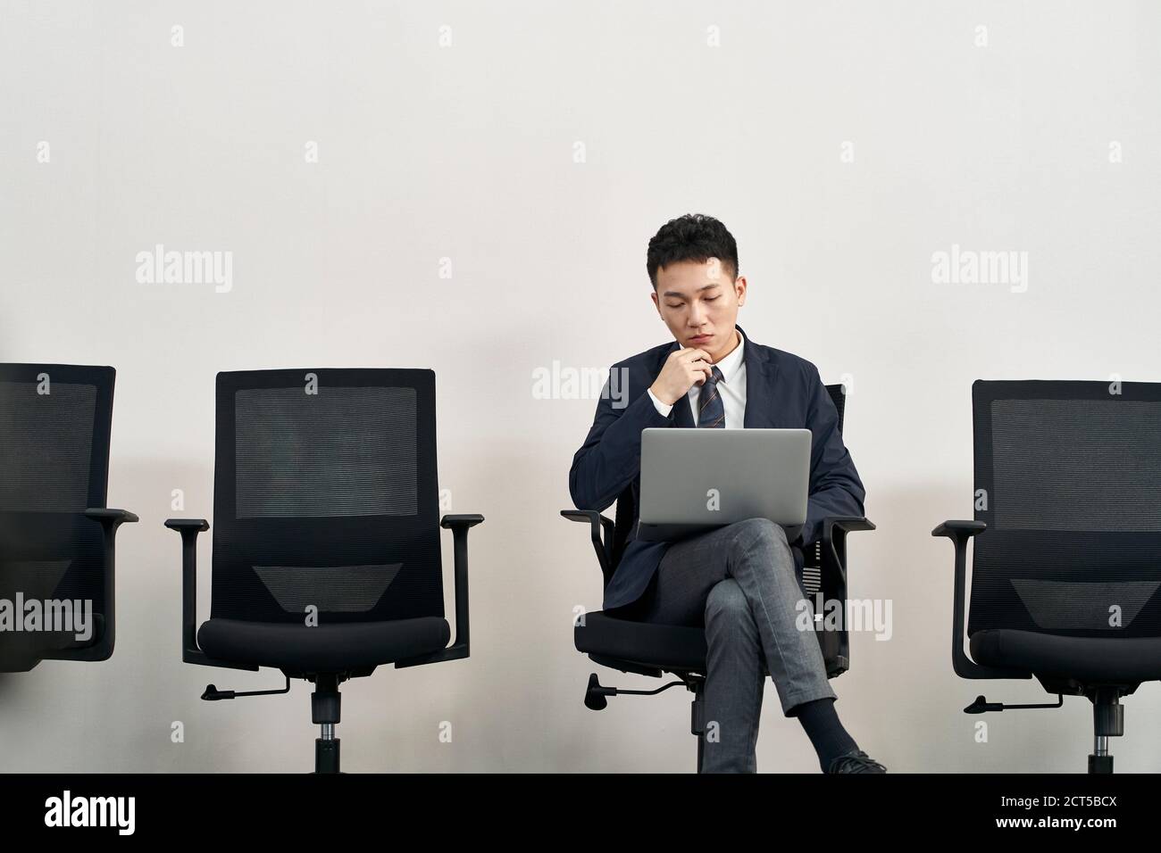giovane cercatore di lavoro asiatico seduto in sedia in preparazione per l'intervista utilizzo di un computer portatile durante l'attesa in linea Foto Stock