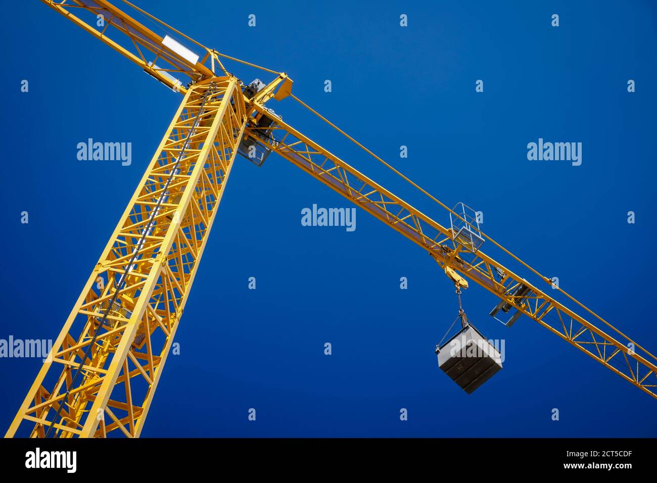 Vista dal basso verso l'alto di una gru gialla che solleva a. peso in un cantiere su un cielo blu piatto sfondo Foto Stock
