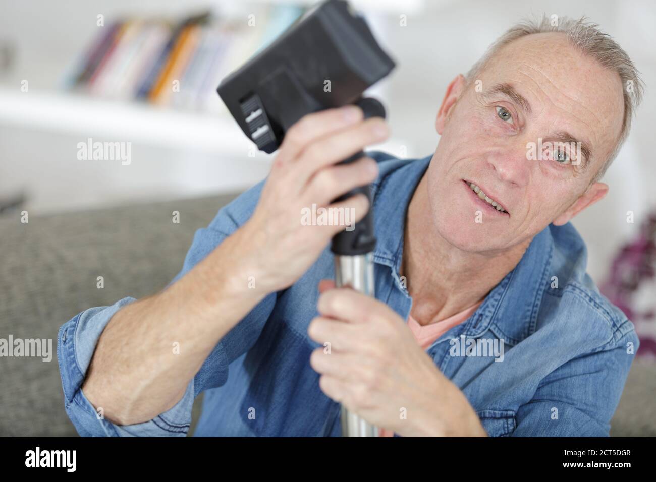 uomo anziano che tiene l'aspirapolvere su un ginocchio tagliato Foto Stock