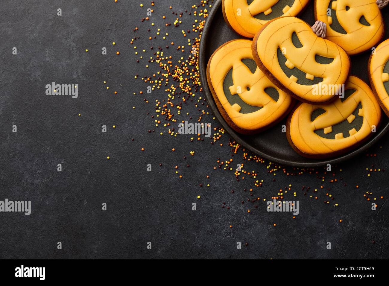 Biscotti di Halloween con pan di zenzero su sfondo nero. Divertenti volti di zucca. Foto Stock