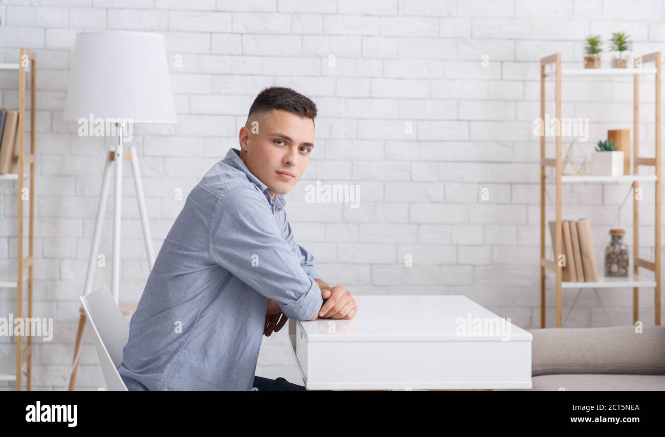 Hobby, tempo libero e registrazione video blog moderno a casa. Un ragazzo serio che guarda la macchina fotografica, seduto al tavolo nell'interno del soggiorno Foto Stock