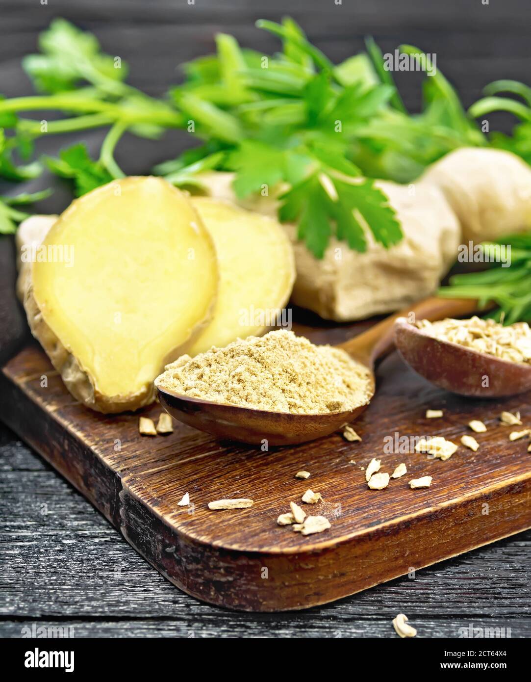 Zenzero macinato e fiocchi in due cucchiai di legno, radice di zenzero, erbe speziate su uno sfondo di legno Foto Stock