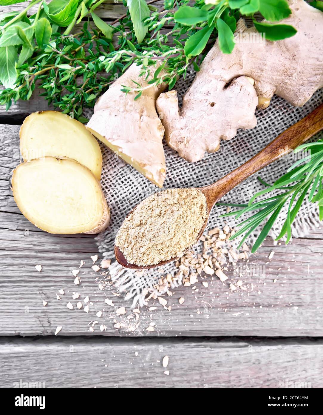 Zenzero macinato in un cucchiaio, fiocchi e radice di zenzero sul burlap, erbe speziate su uno sfondo di una vecchia tavola di legno dall'alto Foto Stock