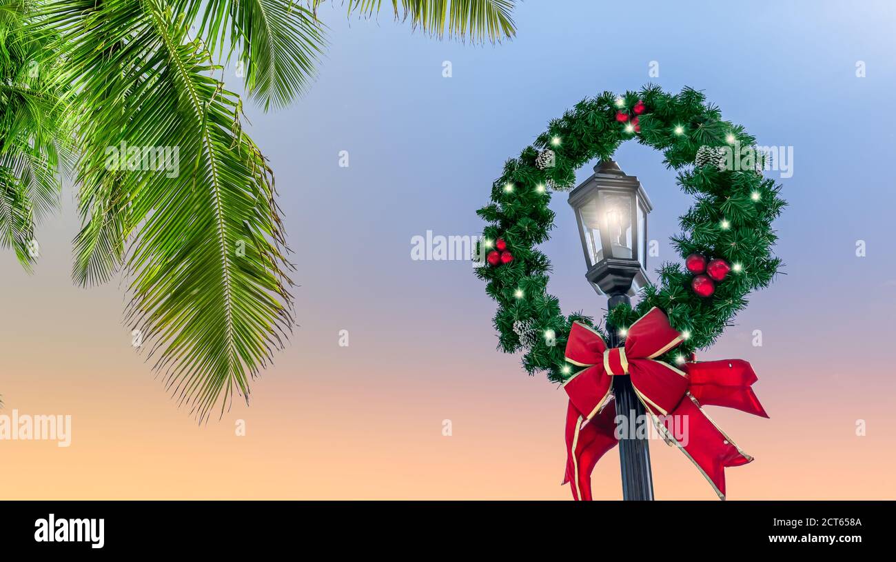 Decorata corona di Natale intorno a un lampione illuminato su una destinazione tropicale. Foto Stock