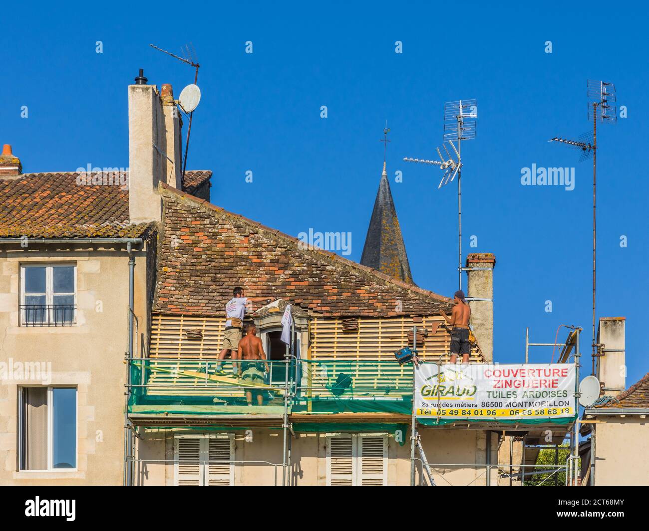 Lavoratori di coperture che sostituiscono i listelli di legno e le piastrelle di argilla in vecchio edificio - Montmorillon, Vienne (86), Francia. Foto Stock