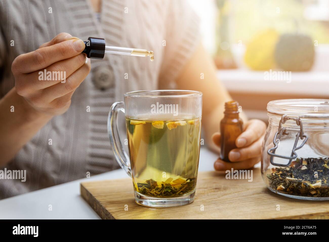 integratori alimentari e vitamine - donna che aggiunge goccia di olio cbd in tazza di tè con pipetta. anti stress Foto Stock