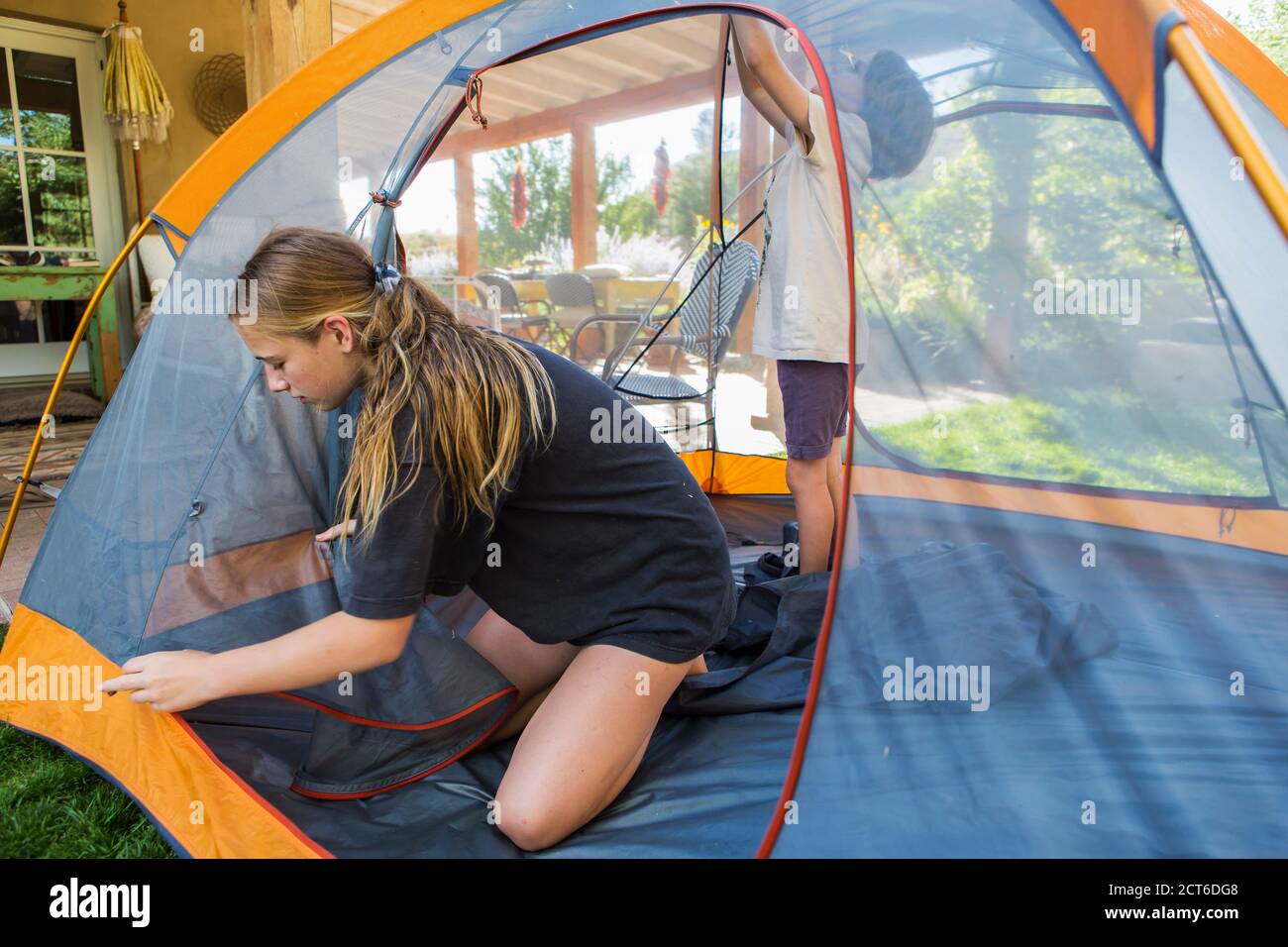 La ragazza adolescente ed il suo fratello più giovane che istituisce la tenda per dormire fuori durante uno staycation. Foto Stock