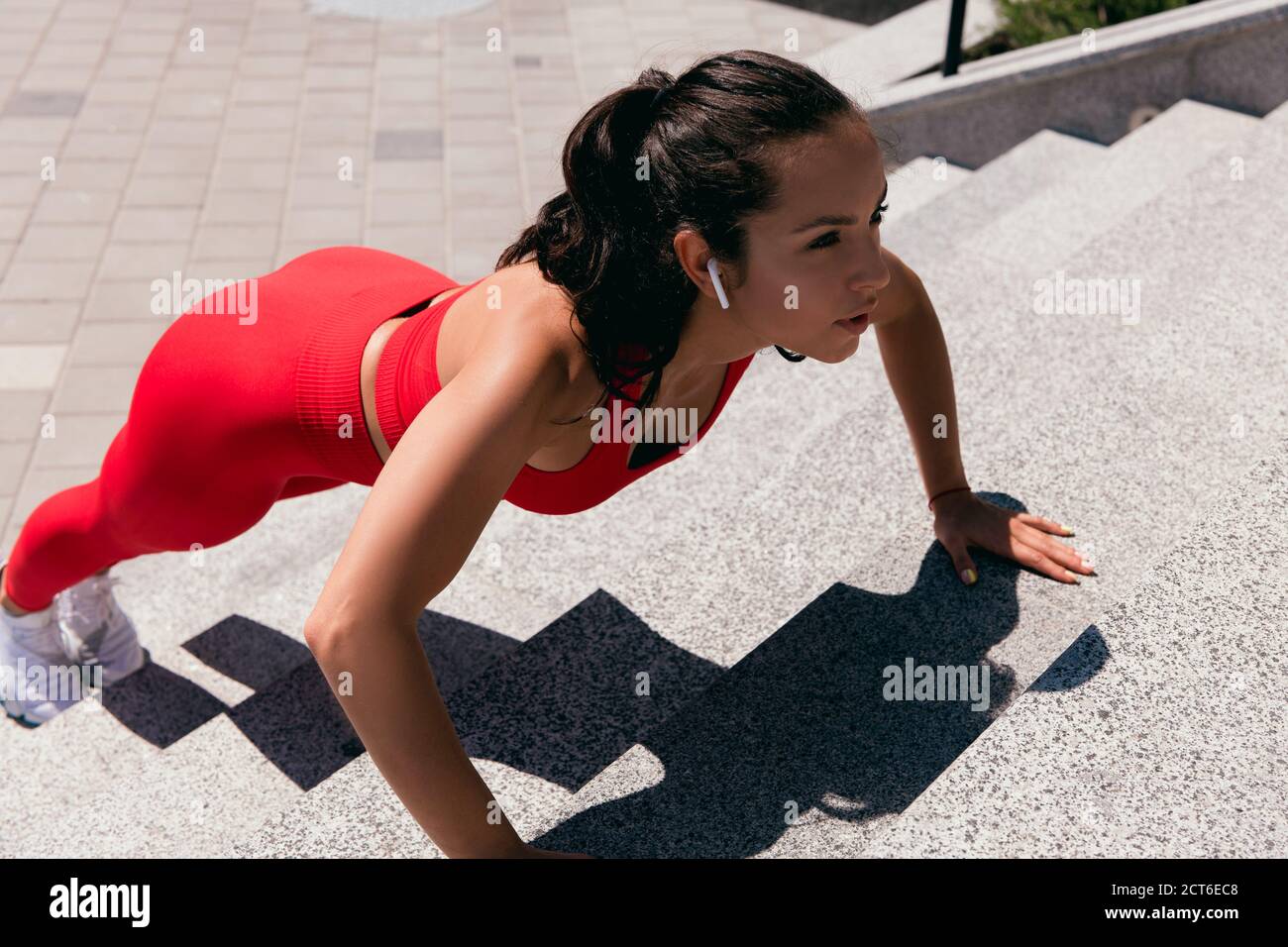 Donna sportiva con coda di coda di rospo scura e scarpe da ginnastica  bianche che si sollevano durante l'ascolto della musica. Bella ragazza  facendo esercizi a mano sulle scale Foto stock -