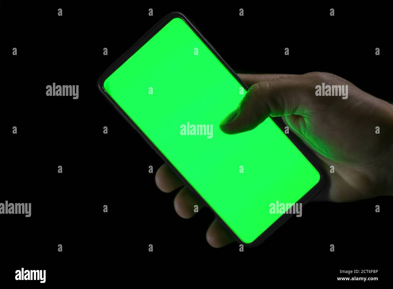 Mano umana isolata che tiene uno smartphone con schermo verde nero background, concetto di dipendenza hi tech Foto Stock